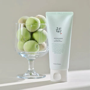 Tube of skincare product next to a glass bowl of green fruits on a neutral background