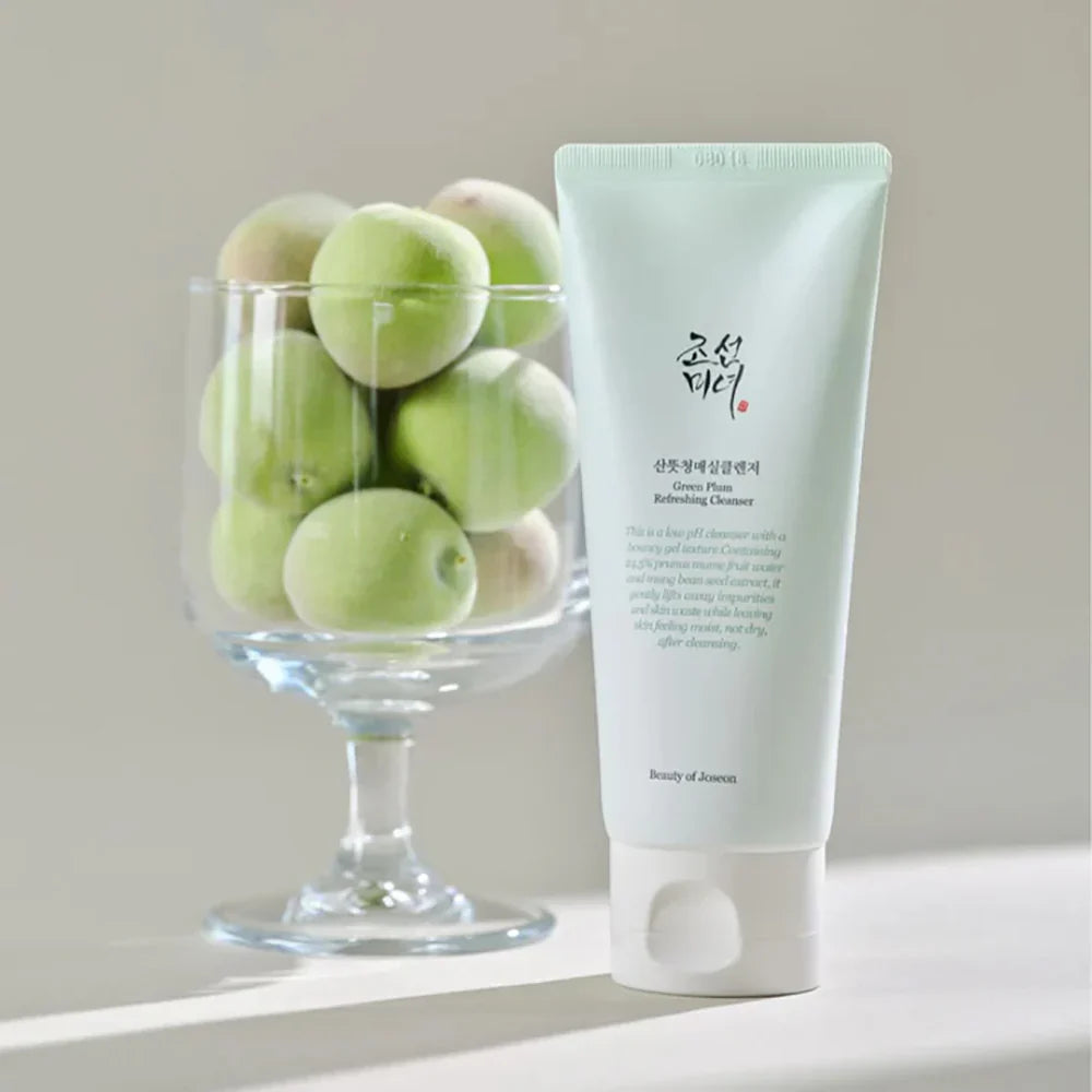 Tube of skincare product next to a glass bowl of green fruits on a neutral background