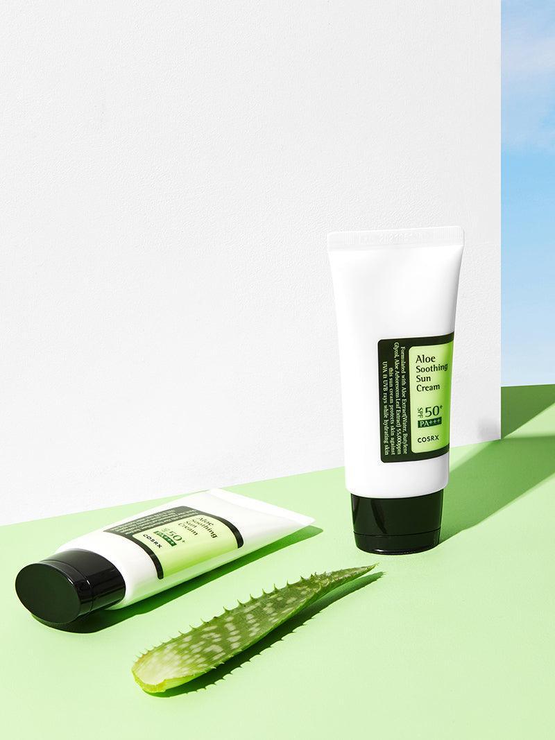 Two tubes of aloe vera cream on a green surface with aloe leaves, against a white and blue gradient background.