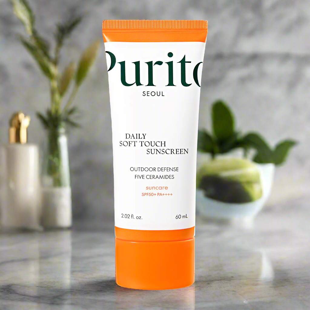 Purito Daily Soft Touch Sunscreen tube on a marble surface with plants in the background