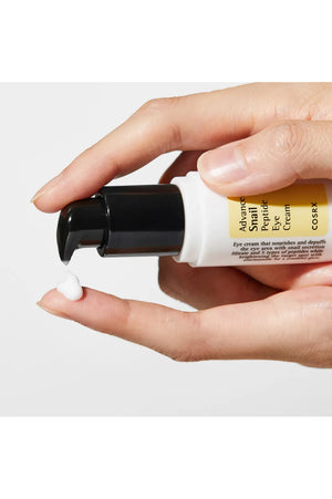 Hand holding a tube of COSRX Advanced Snail Repair Eye Cream on a white background